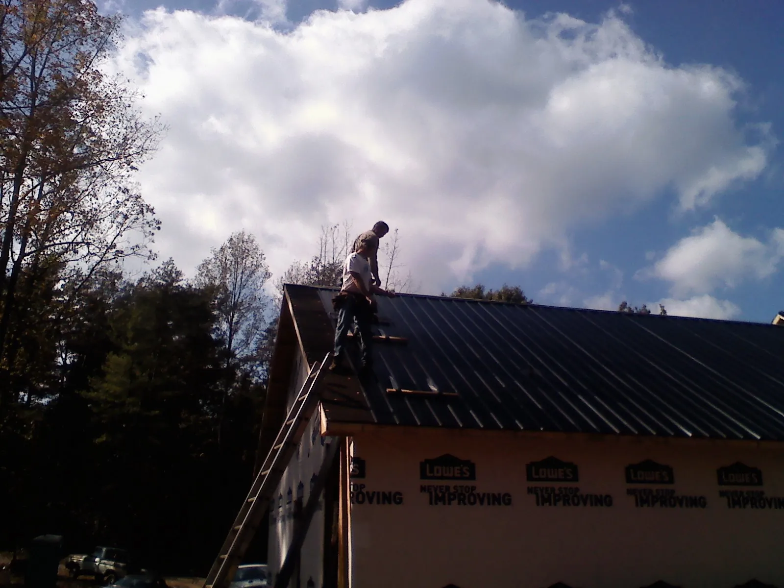 Roofer fastening dark metal panels high against a cloudy sky, from a Roof Inspection job in Eloy